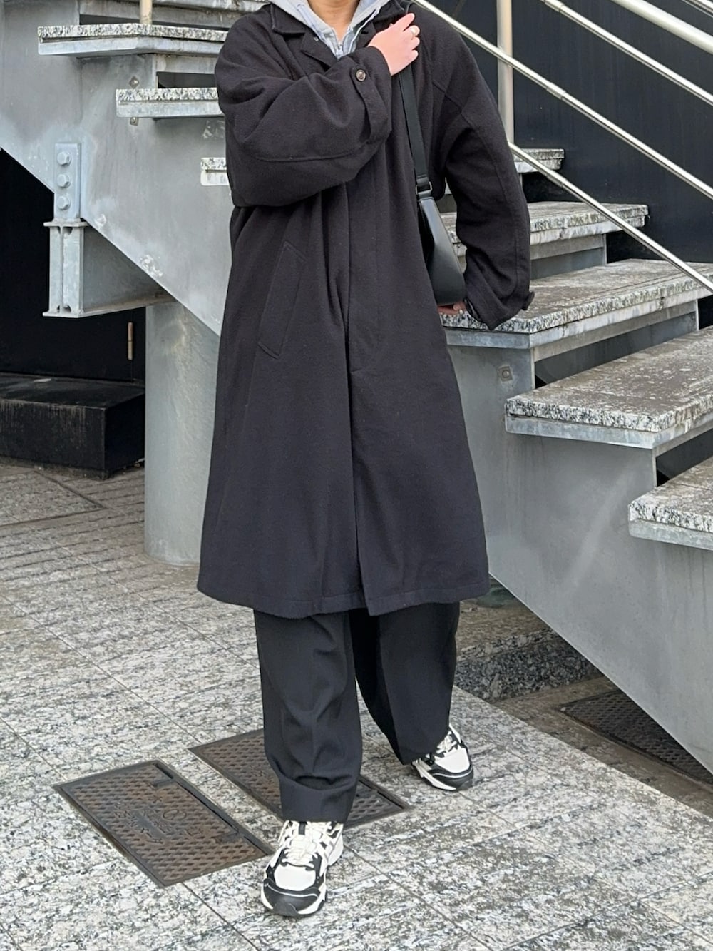 ブラック系のステンカラーコート、ブラック系のショルダーバッグ、グレー系のパーカーを着用したメンズの冬コーディネートの3枚目の写真