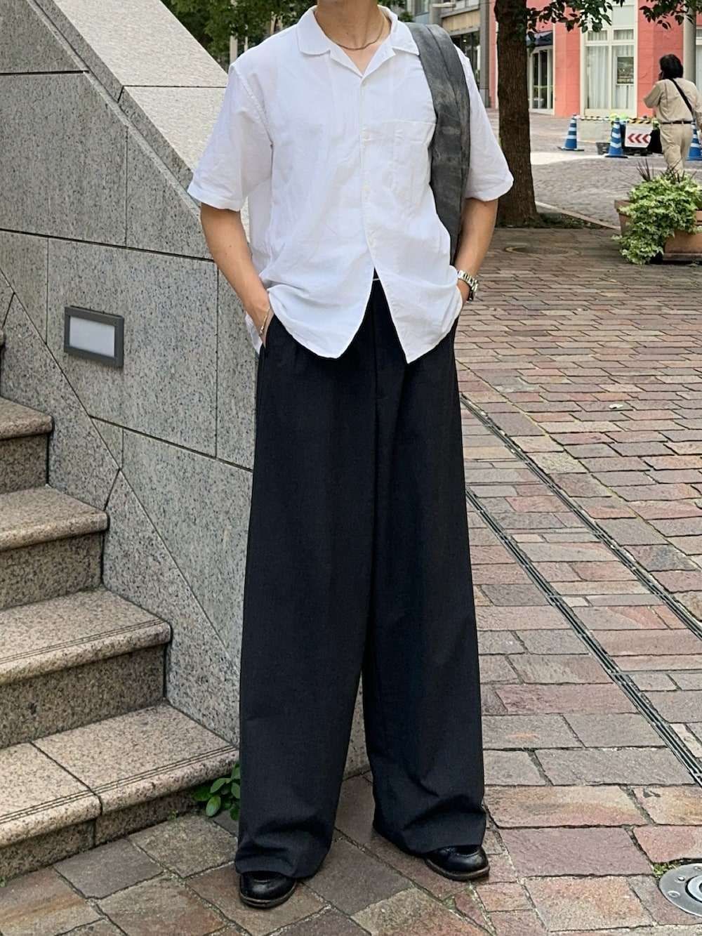 グレー系のショルダーバッグ、グレー系のスラックス、ブラック系のローファーを着用したメンズの夏コーディネートの2枚目の写真