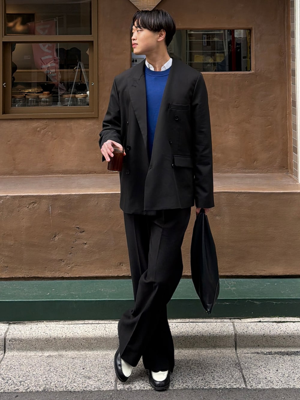 ブラック系のテーラードジャケット、ブルー系のニット/セーター、ブラック系のトートバッグを着用したメンズの春コーディネートの2枚目の写真