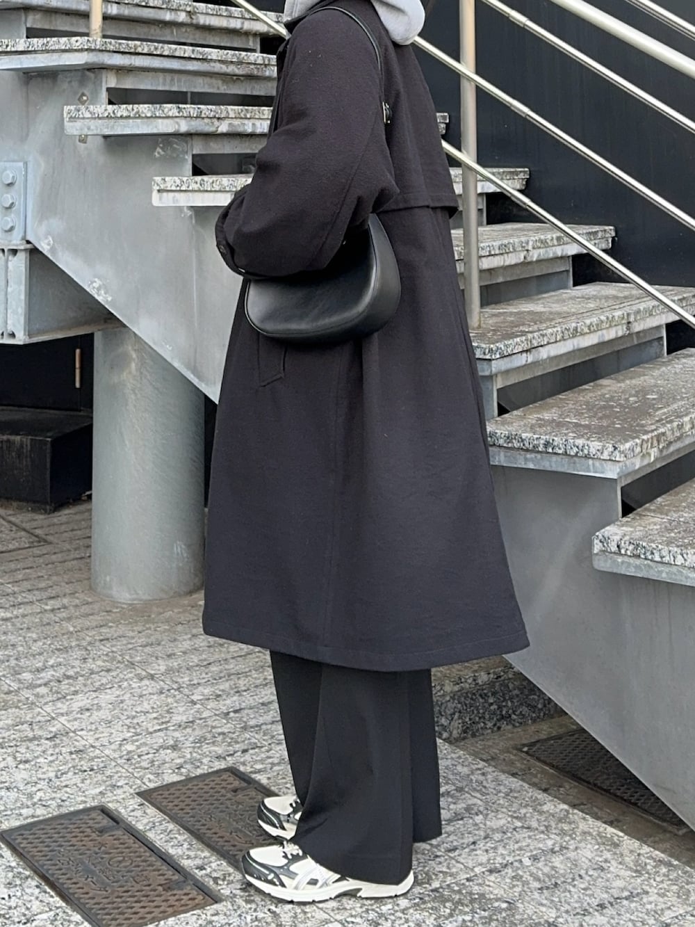 ブラック系のステンカラーコート、ブラック系のショルダーバッグ、グレー系のパーカーを着用したメンズの冬コーディネートの4枚目の写真