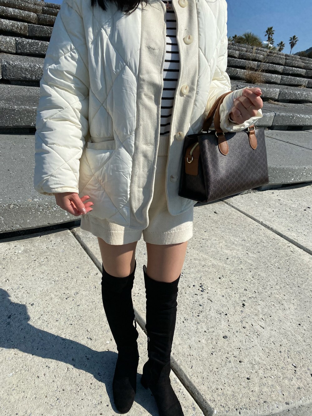 ブラック系のブーツ、ベージュ系のパンツ、ホワイト系のジャケット/アウターを着用したレディースの冬コーディネートの2枚目の写真