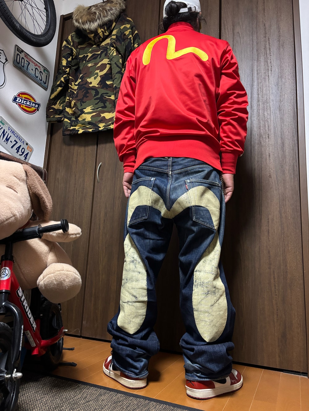 レッド系のスカジャン、ブルー系のデニムパンツ、ホワイト系のスニーカーを着用したメンズの夏コーディネートの2枚目の写真