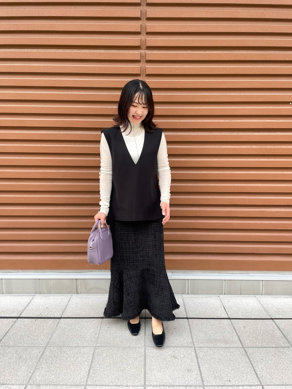 ブラック系のスカート、パープル系のボストンバッグ、ブラック系のパンプスを着用したレディースの秋コーディネートの2枚目の写真