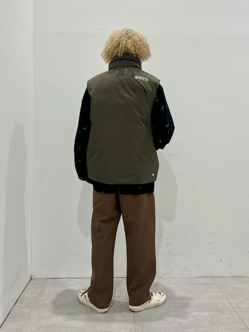 グリーン系のダウンベスト、ブラック系のカバーオール、ブラウン系のスラックスを着用したメンズの秋コーディネートの3枚目の写真