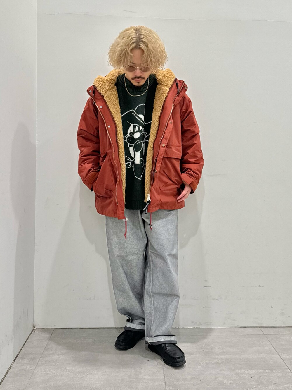 オレンジ系のマウンテンパーカー、グリーン系のニット/セーター、グレー系のパンツを着用したメンズの秋コーディネートの2枚目の写真