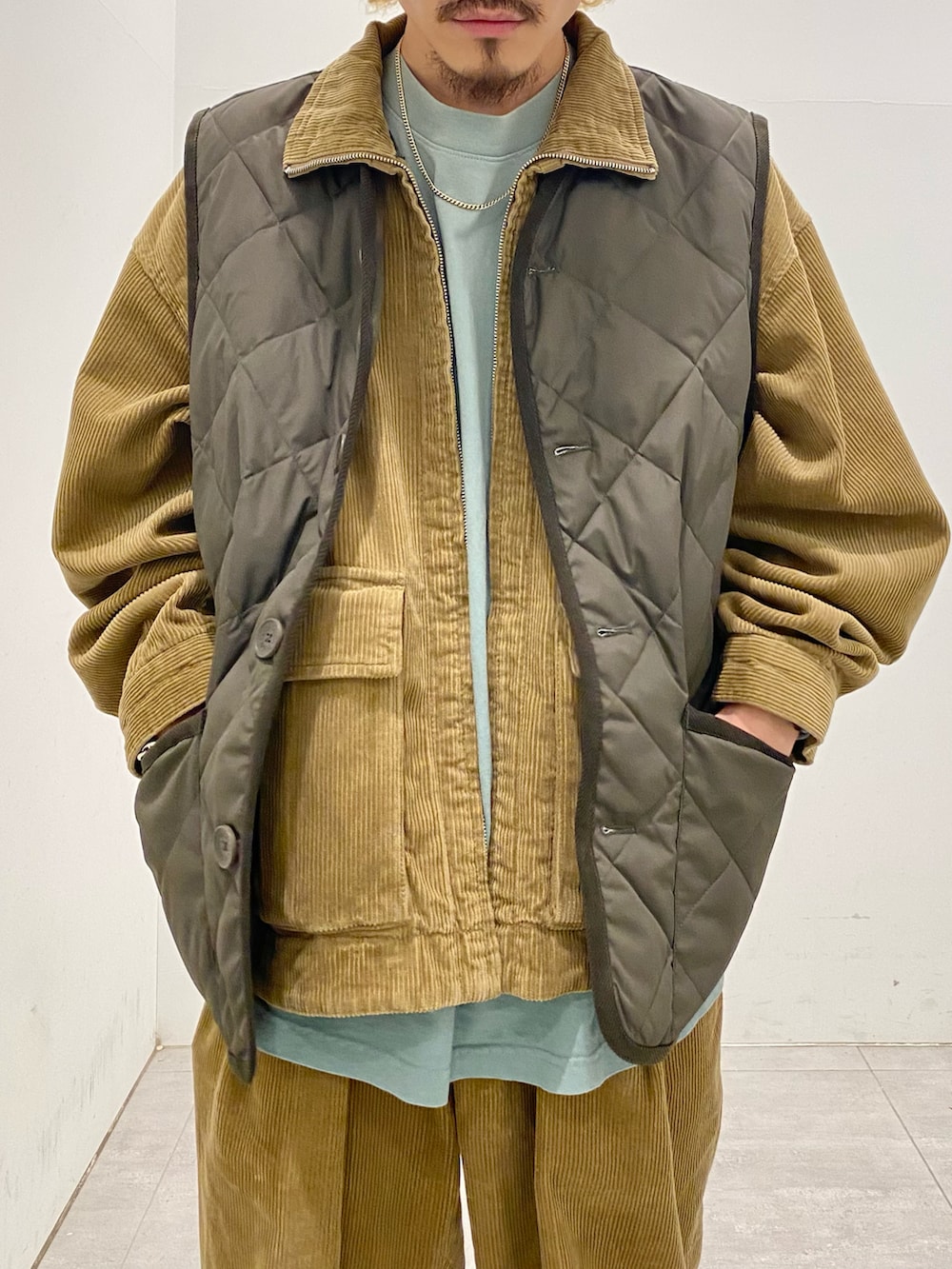 グリーン系のダウンベスト、イエロー系のブルゾン、イエロー系のスラックスを着用したメンズの秋コーディネートの3枚目の写真