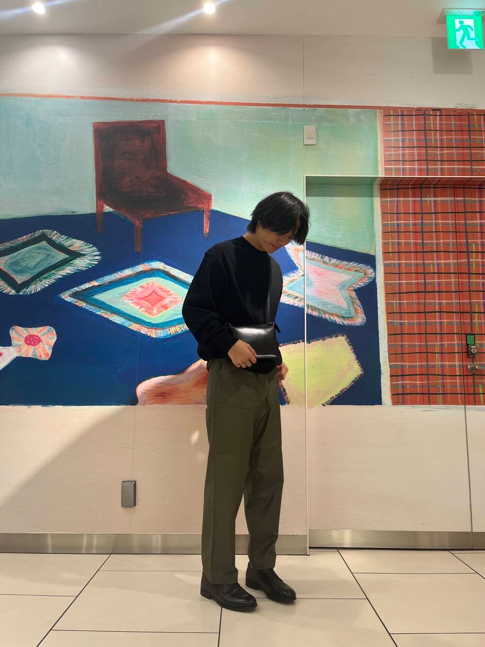 ブラック系のショルダーバッグ、ブラック系のニット/セーター、グリーン系のチノパンツを着用したメンズの夏コーディネートの2枚目の写真