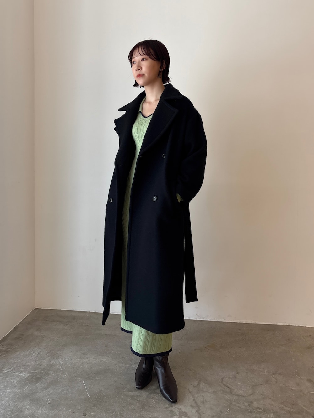 グリーン系のワンピース、ブラック系のステンカラーコート、ブラウン系のブーツを着用したレディースの秋コーディネートの2枚目の写真