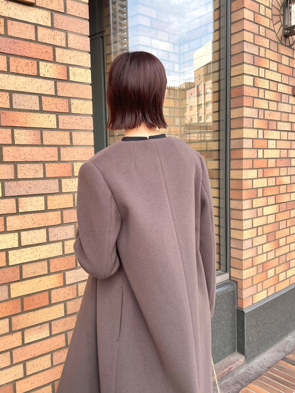 グレー系のノーカラーコート、ブラック系のドレス、シルバー系のハンドバッグを着用したレディースの秋コーディネートの6枚目の写真