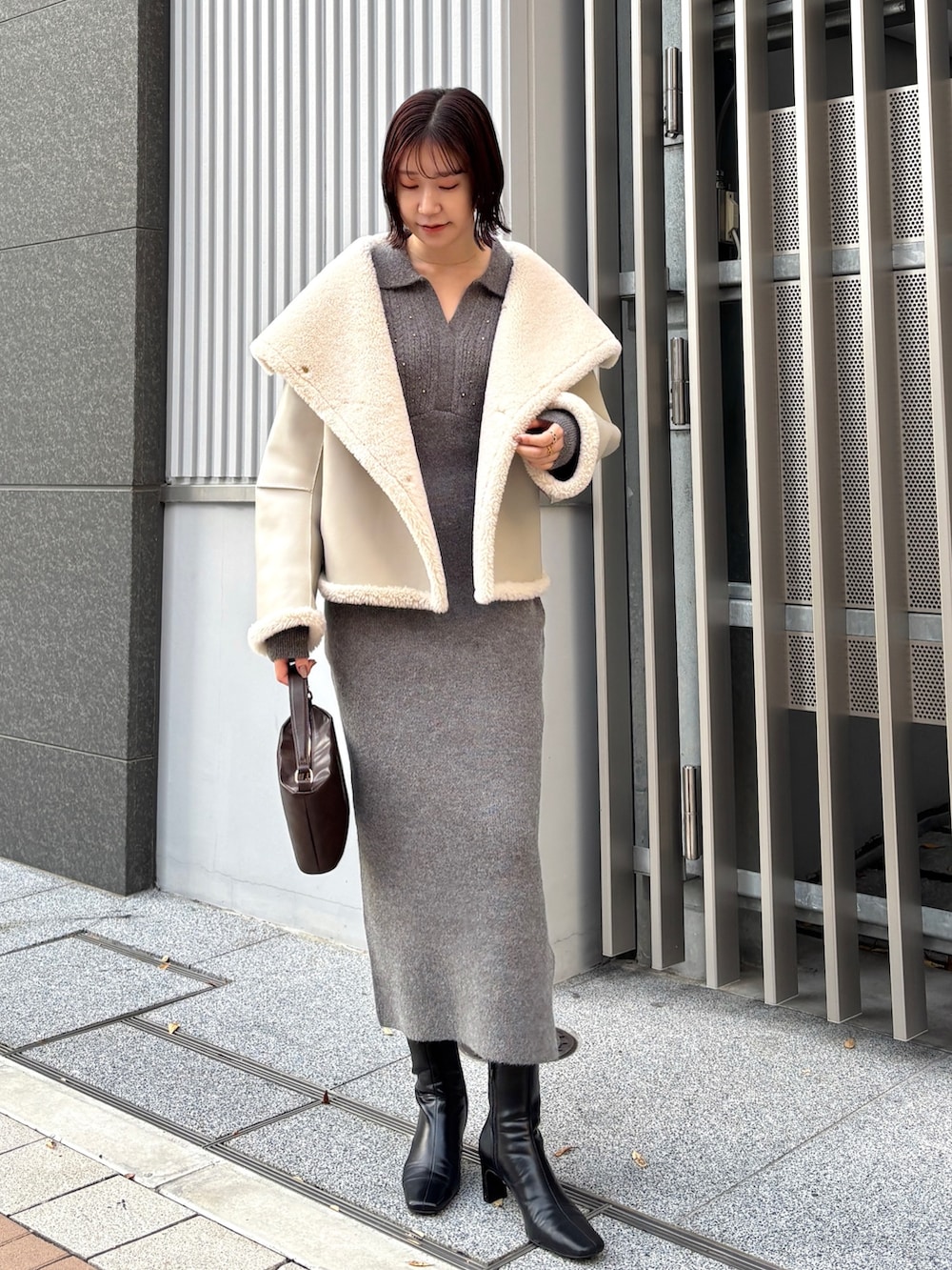 グレー系のワンピース、ブラウン系のハンドバッグ、ブラック系のブーツを着用したレディースの冬コーディネートの6枚目の写真