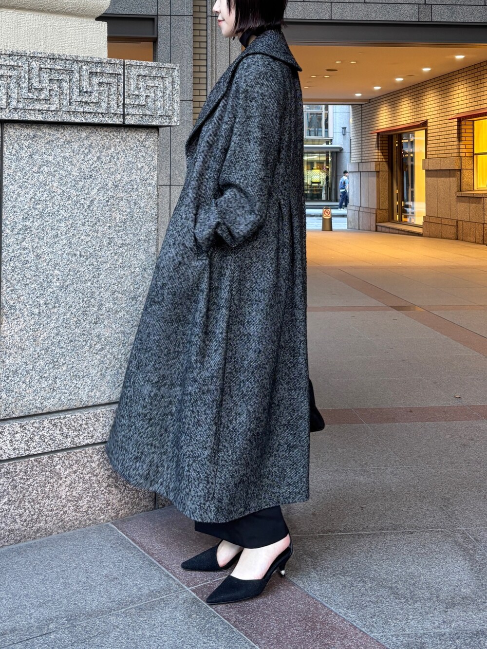 ブラック系のドレス、ブラック系のチェスターコート、ブラック系のハンドバッグを着用したレディースの冬コーディネートの2枚目の写真