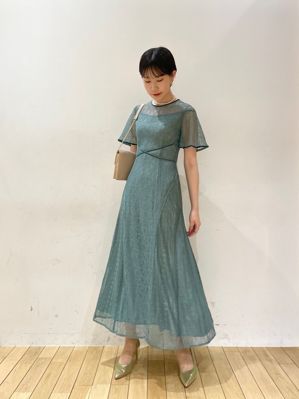 グリーン系のドレス、ベージュ系のクラッチバッグ、ゴールド系のパンプスを着用したレディースの冬コーディネートの3枚目の写真