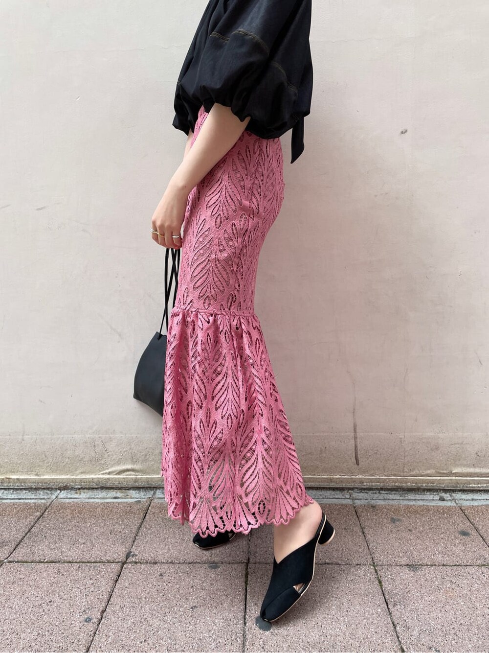 ブラック系のハンドバッグ、ブラック系のサンダル、ピンク系のスカートを着用したレディースの春コーディネートの6枚目の写真