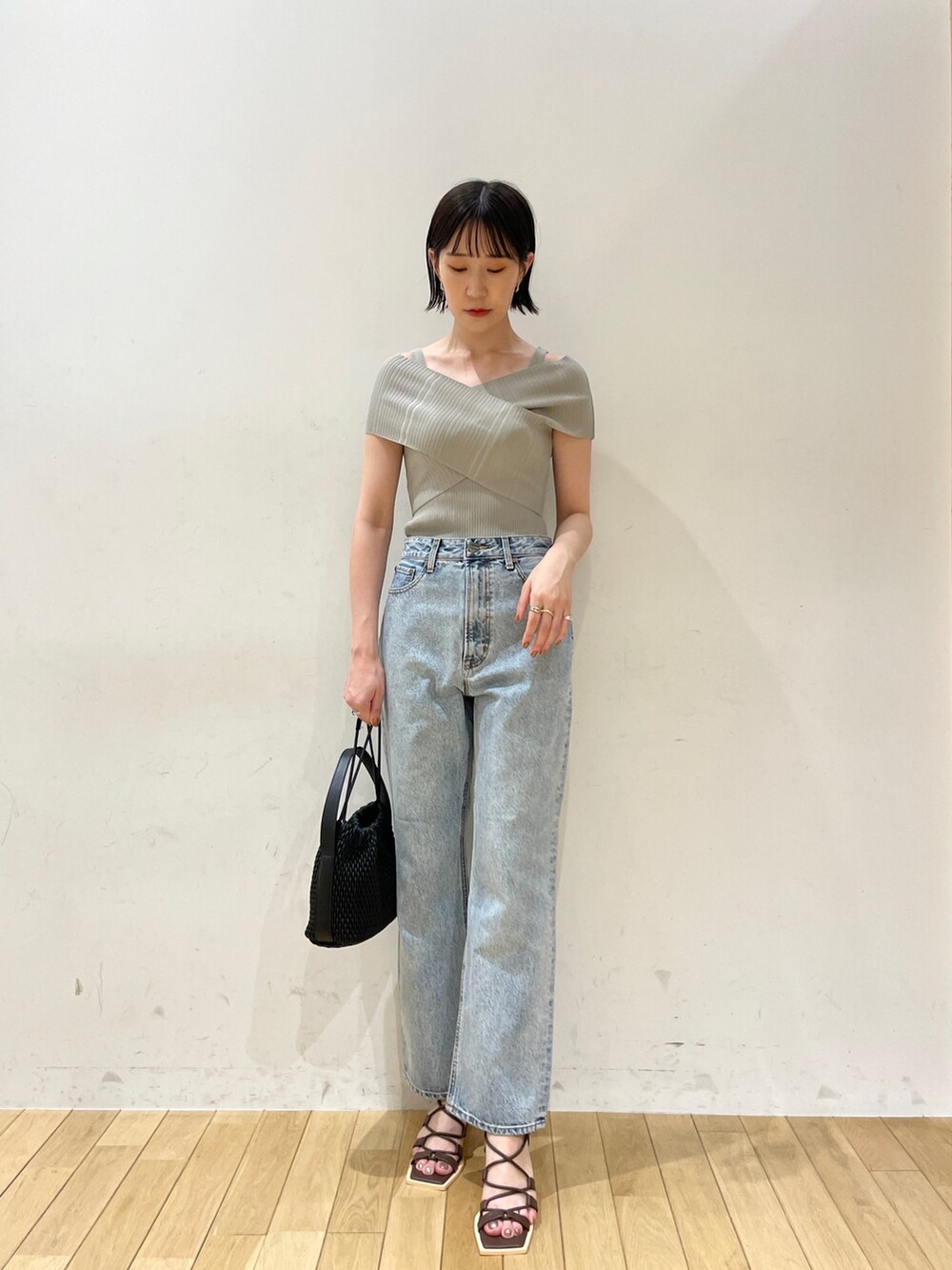 グリーン系のニット/セーター、ブルー系のデニムパンツ、ブラック系のハンドバッグを着用したレディースの夏コーディネートの2枚目の写真