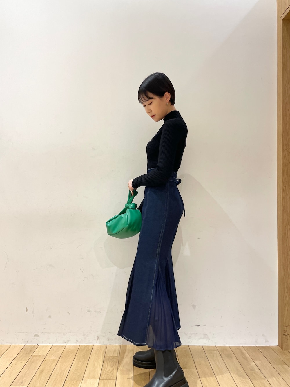 ブルー系のスカート、ブラック系のニット/セーター、グリーン系のハンドバッグを着用したレディースの冬コーディネートの3枚目の写真