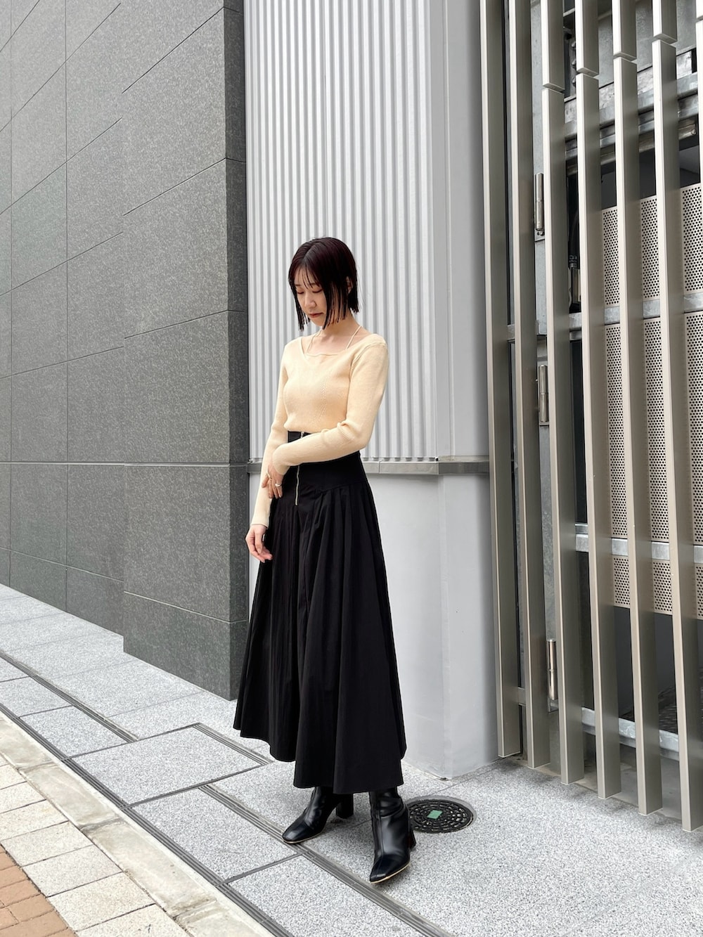 ブラック系のブーツ、ホワイト系のニット/セーター、ブラック系のスカートを着用したレディースの冬コーディネートの2枚目の写真