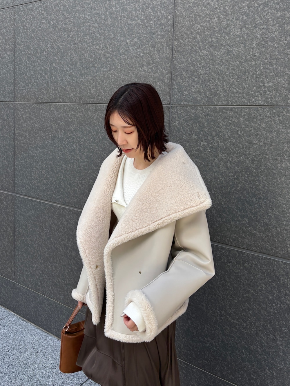 ホワイト系のムートンコート、ホワイト系のアンサンブル、イエロー系のハンドバッグを着用したレディースの冬コーディネートの6枚目の写真