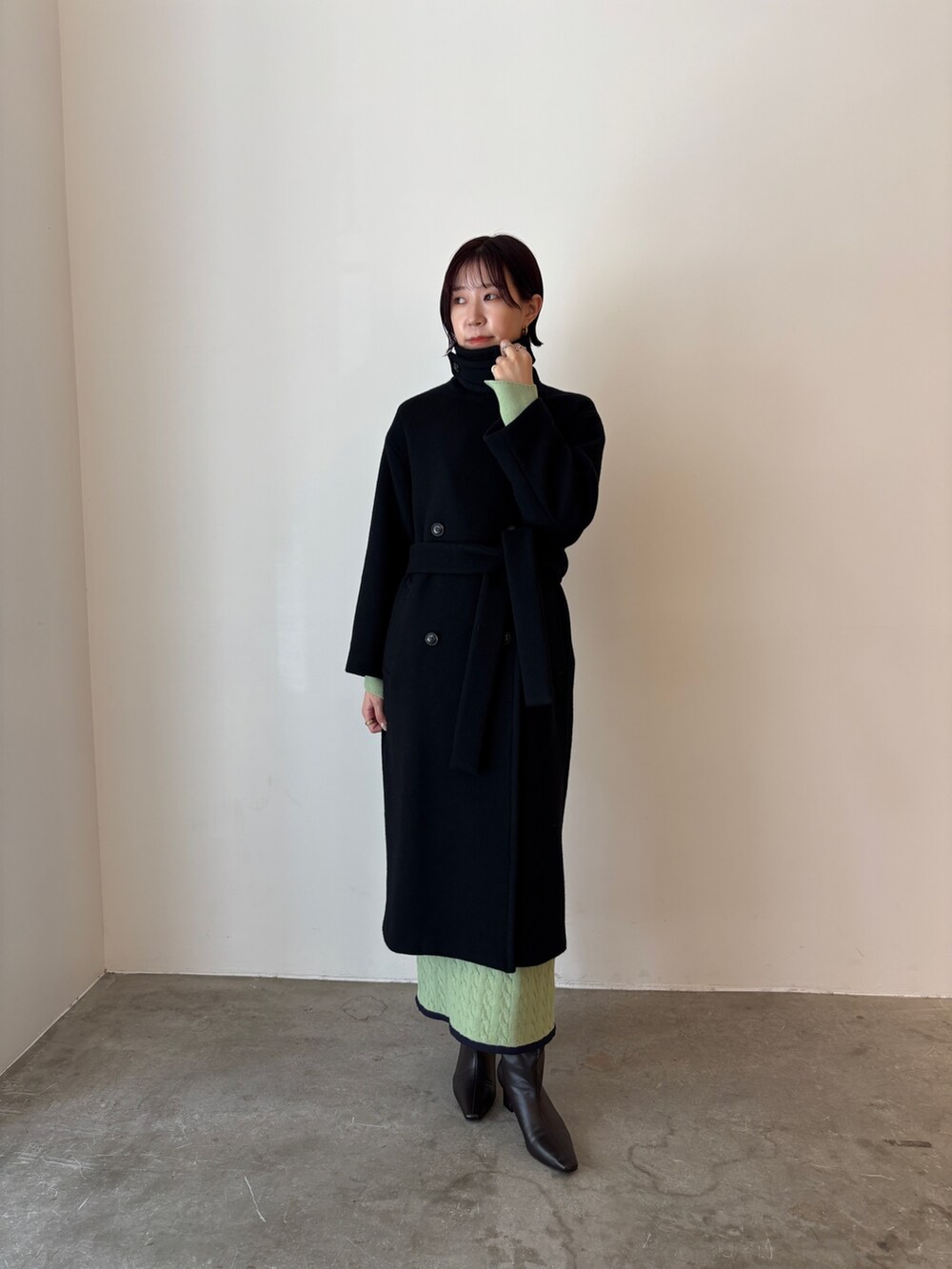 グリーン系のワンピース、ブラック系のステンカラーコート、ブラウン系のブーツを着用したレディースの秋コーディネートの4枚目の写真