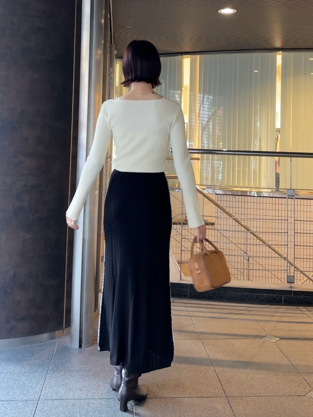 イエロー系のハンドバッグ、ブラウン系のブーツ、ホワイト系のニット/セーターを着用したレディースの冬コーディネートの3枚目の写真