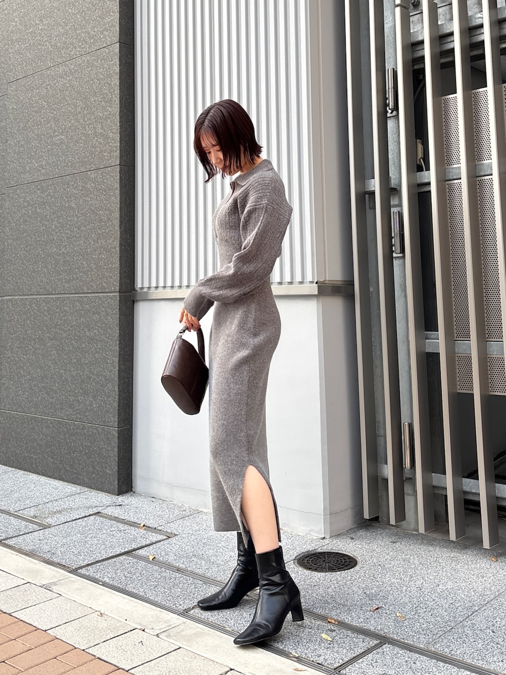 グレー系のワンピース、ブラウン系のハンドバッグ、ブラック系のブーツを着用したレディースの冬コーディネートの2枚目の写真