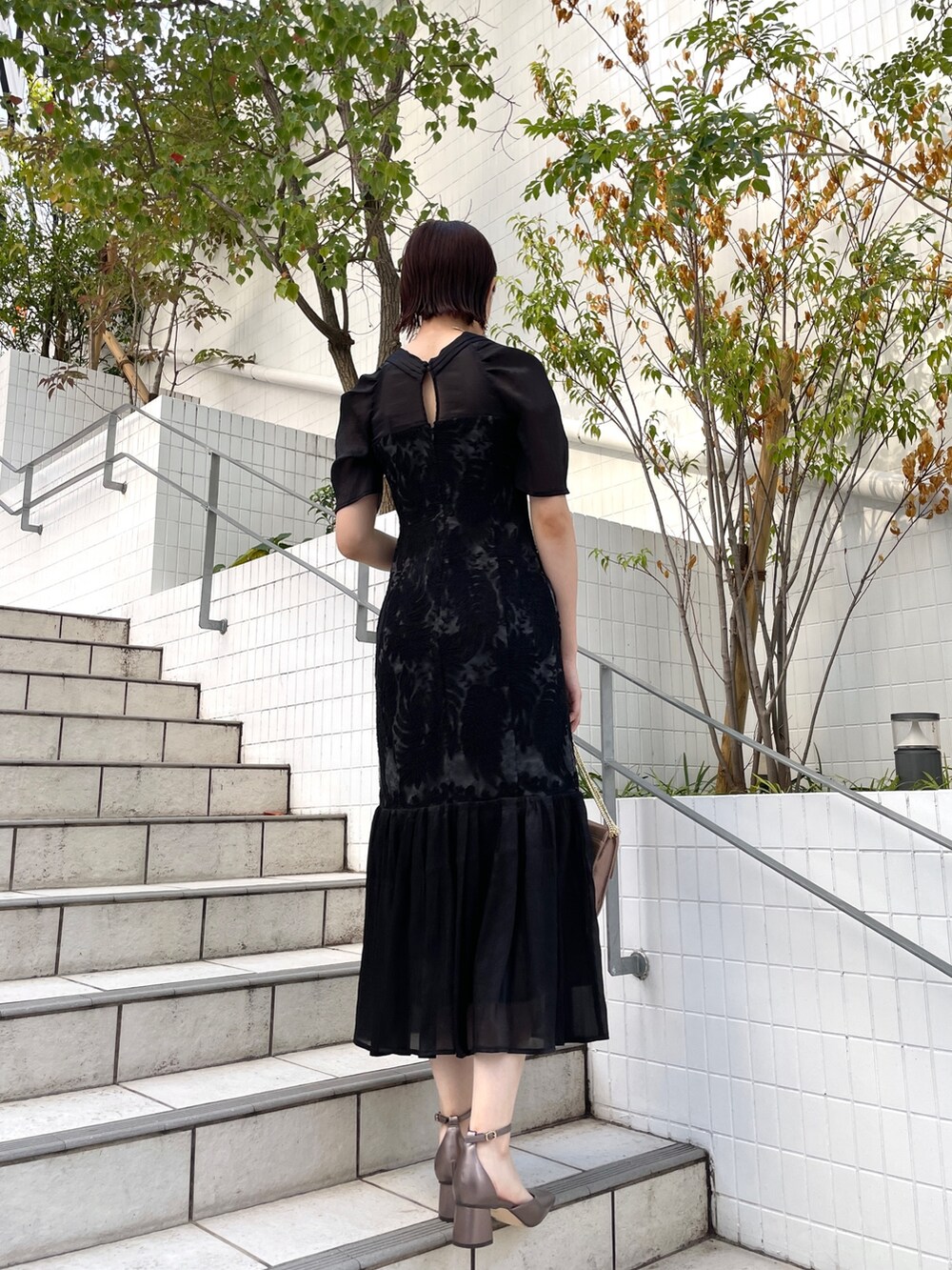 ゴールド系のハンドバッグ、その他のパンプス、ブラック系のドレスを着用したレディースの秋コーディネートの3枚目の写真