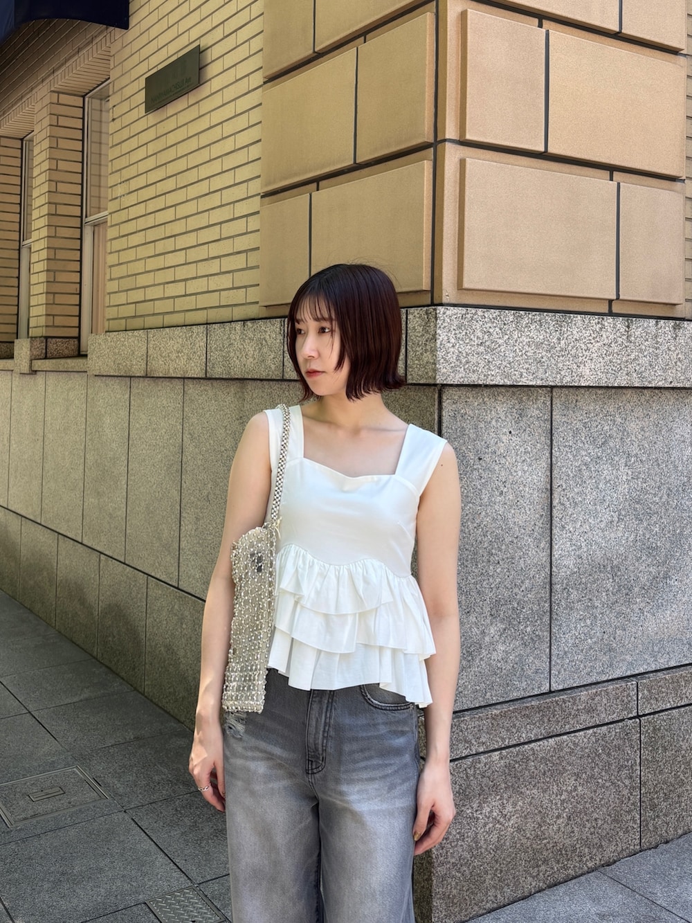 グレー系のデニムパンツ、ホワイト系のハンドバッグ、ホワイト系のサンダルを着用したレディースの春コーディネートの5枚目の写真