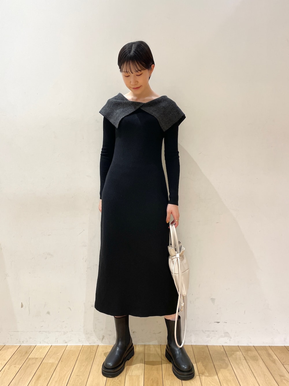 ブラック系のワンピース、ホワイト系のハンドバッグ、ブラック系のブーツを着用したレディースの冬コーディネートの2枚目の写真