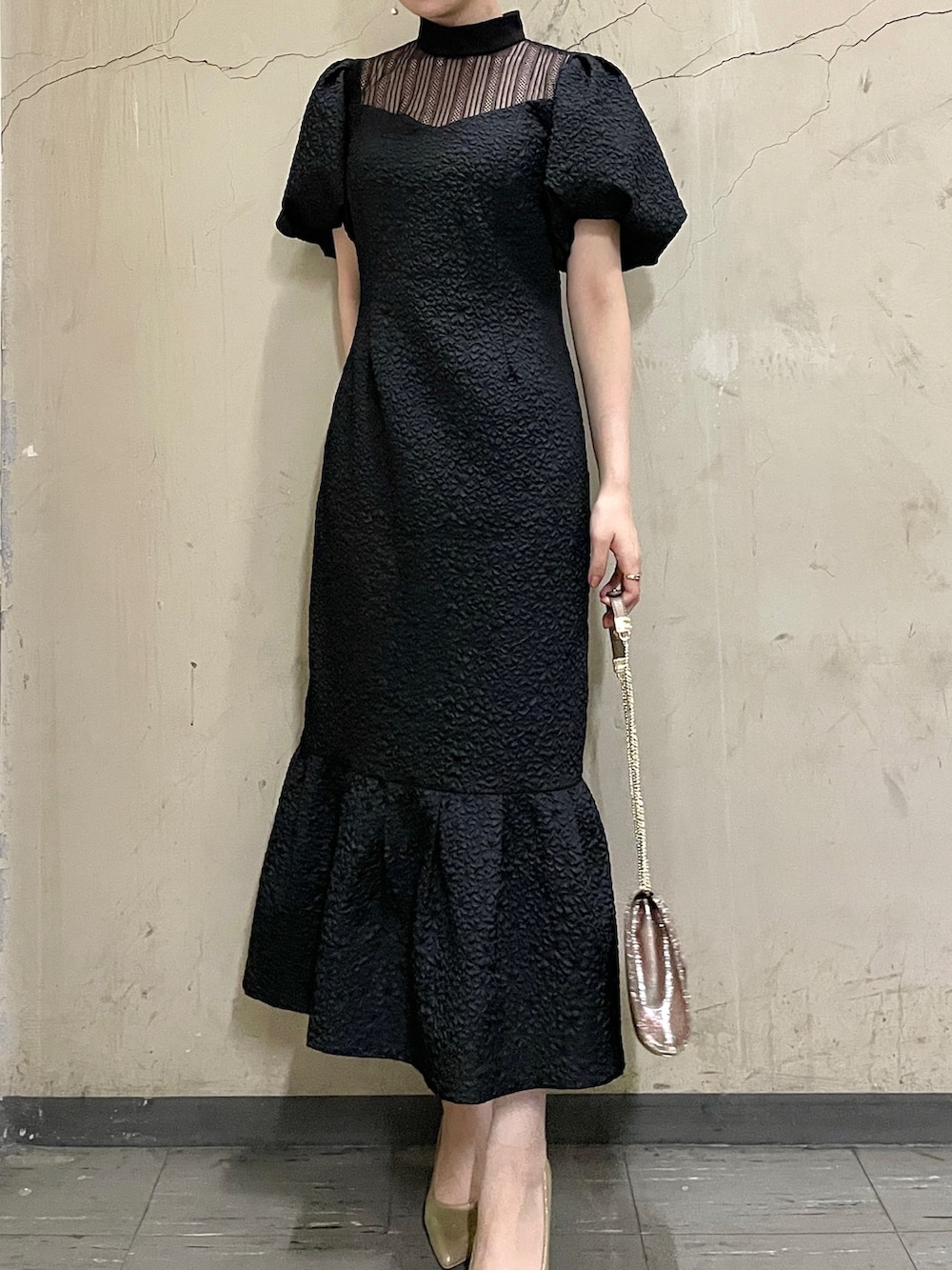 ブラック系のドレス、ゴールド系のハンドバッグ、ゴールド系のパンプスを着用したレディースの秋コーディネートの5枚目の写真