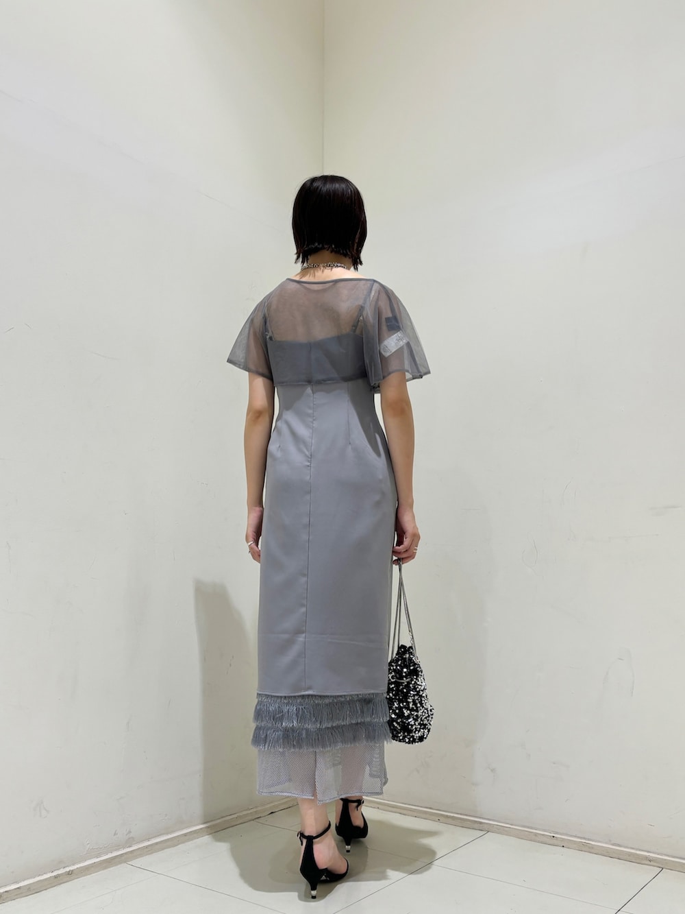 シルバー系のハンドバッグ、ブラック系のパンプス、パープル系のドレスを着用したレディースの夏コーディネートの3枚目の写真