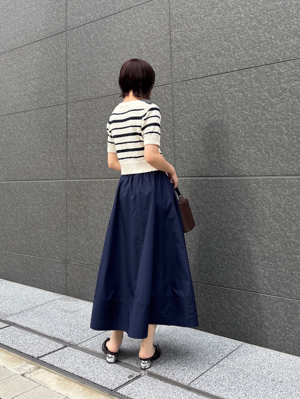 ブルー系のスカート、ホワイト系のニット/セーター、ブラウン系のハンドバッグを着用したレディースの春コーディネートの3枚目の写真