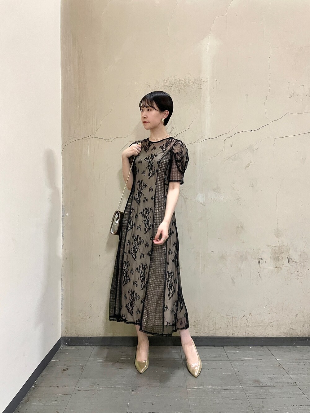 ブラック系のドレス、ゴールド系のハンドバッグ、ゴールド系のパンプスを着用したレディースの秋コーディネートの2枚目の写真