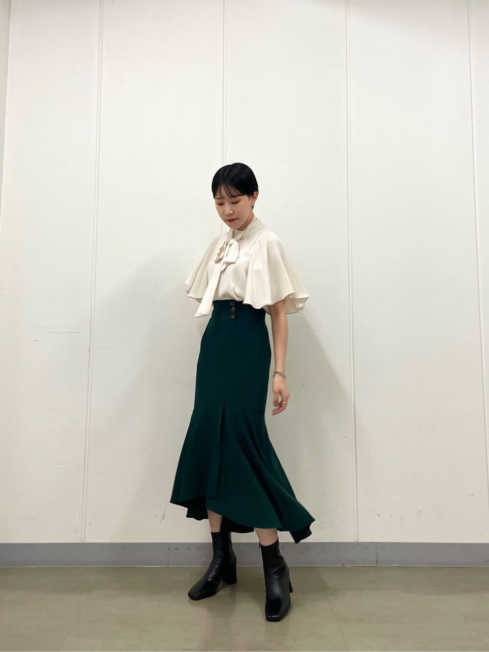 ホワイト系のシャツ/ブラウス、グリーン系のスカート、ブラック系のブーツを着用したレディースの秋コーディネートの2枚目の写真