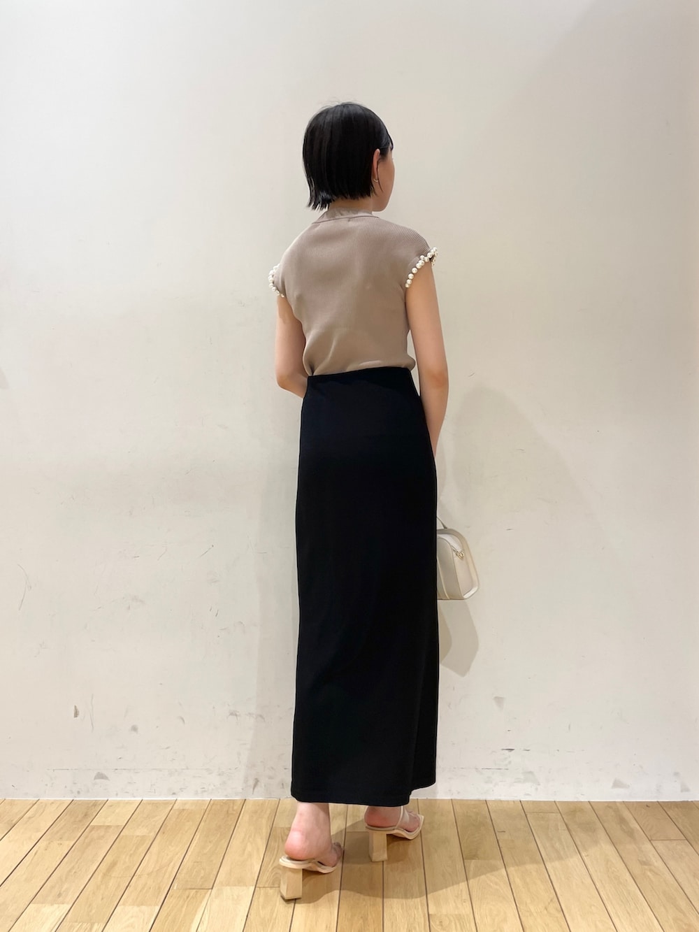 ブラック系のスカート、ベージュ系のニット/セーター、ホワイト系のショルダーバッグを着用したレディースの夏コーディネートの3枚目の写真