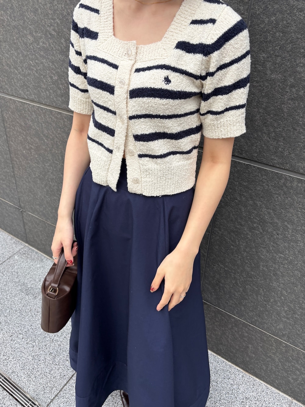 ブルー系のスカート、ホワイト系のニット/セーター、ブラウン系のハンドバッグを着用したレディースの春コーディネートの5枚目の写真