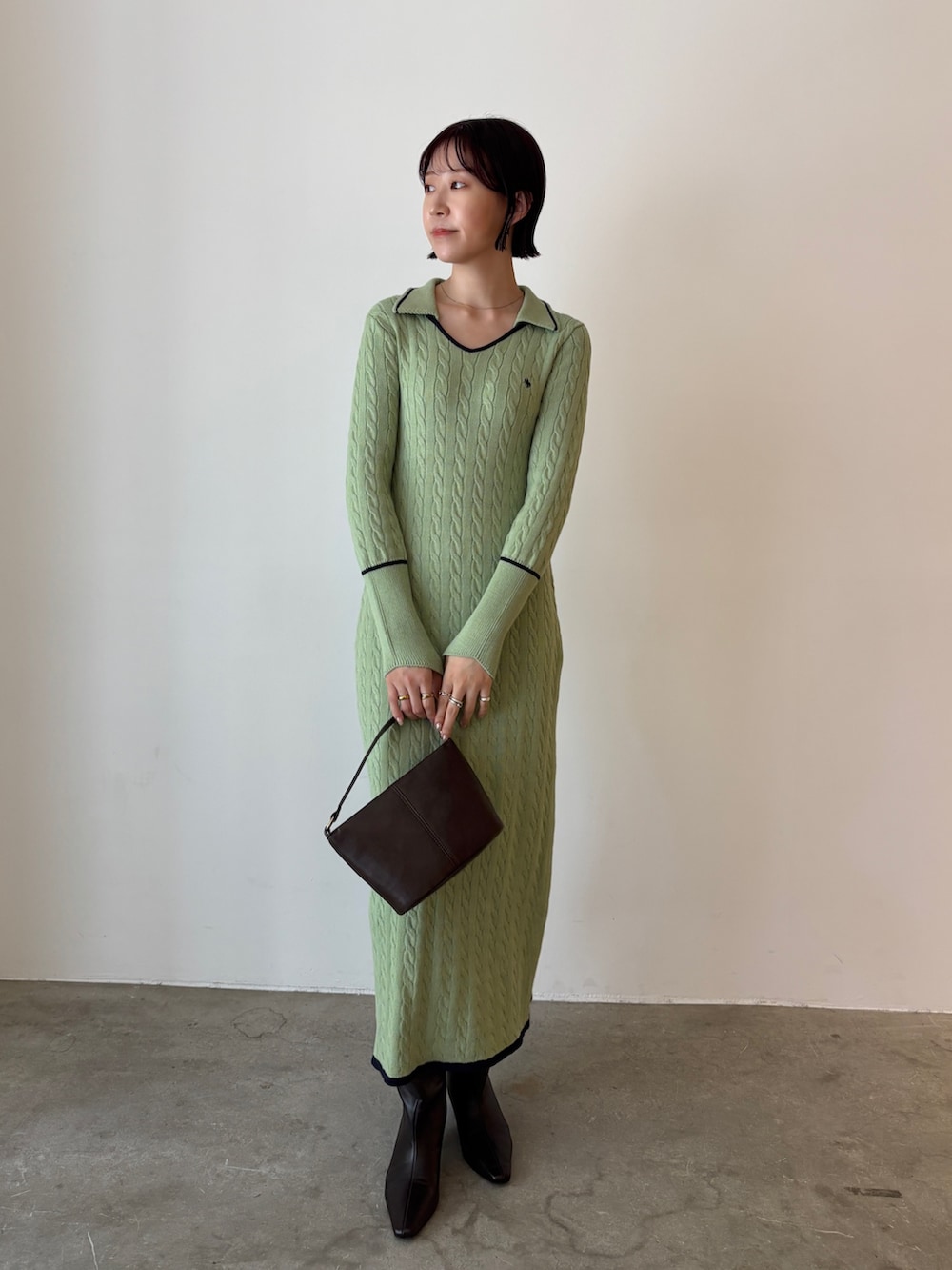 グリーン系のワンピース、ブラウン系のハンドバッグ、ブラウン系のブーツを着用したレディースの秋コーディネートの2枚目の写真