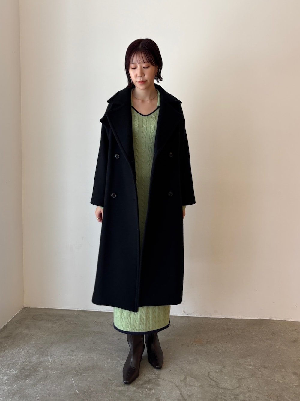 グリーン系のワンピース、ブラック系のステンカラーコート、ブラウン系のブーツを着用したレディースの秋コーディネートの3枚目の写真