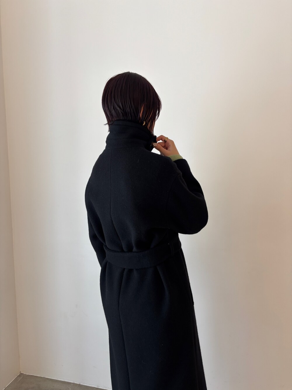 グリーン系のワンピース、ブラック系のステンカラーコート、ブラウン系のブーツを着用したレディースの秋コーディネートの7枚目の写真