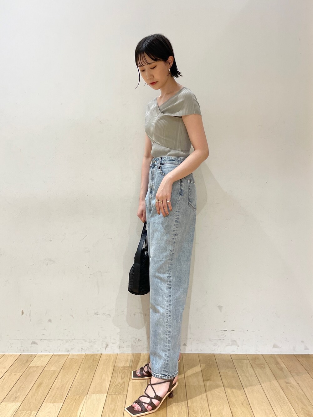 グリーン系のニット/セーター、ブルー系のデニムパンツ、ブラック系のハンドバッグを着用したレディースの夏コーディネートの3枚目の写真