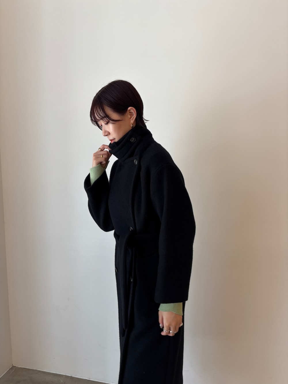 グリーン系のワンピース、ブラック系のステンカラーコート、ブラウン系のブーツを着用したレディースの秋コーディネートの5枚目の写真