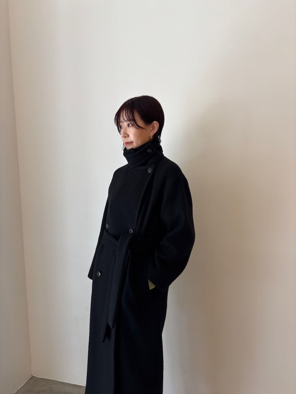 グリーン系のワンピース、ブラック系のステンカラーコート、ブラウン系のブーツを着用したレディースの秋コーディネートの6枚目の写真