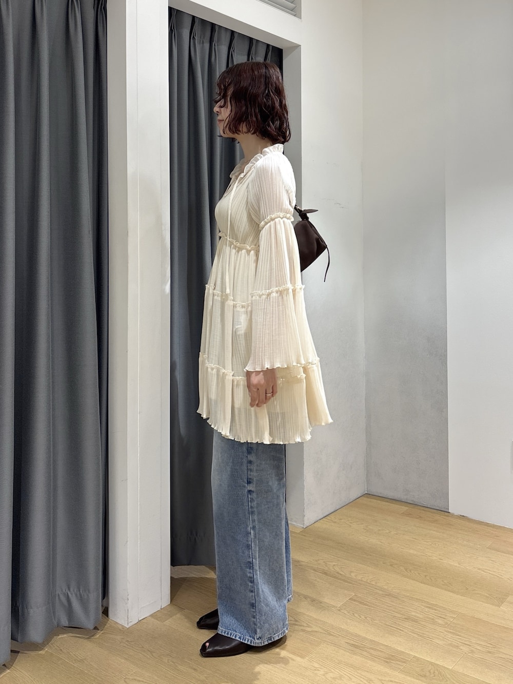 ホワイト系のワンピース、ブルー系のデニムパンツ、ブラウン系のハンドバッグを着用したレディースの秋コーディネートの3枚目の写真