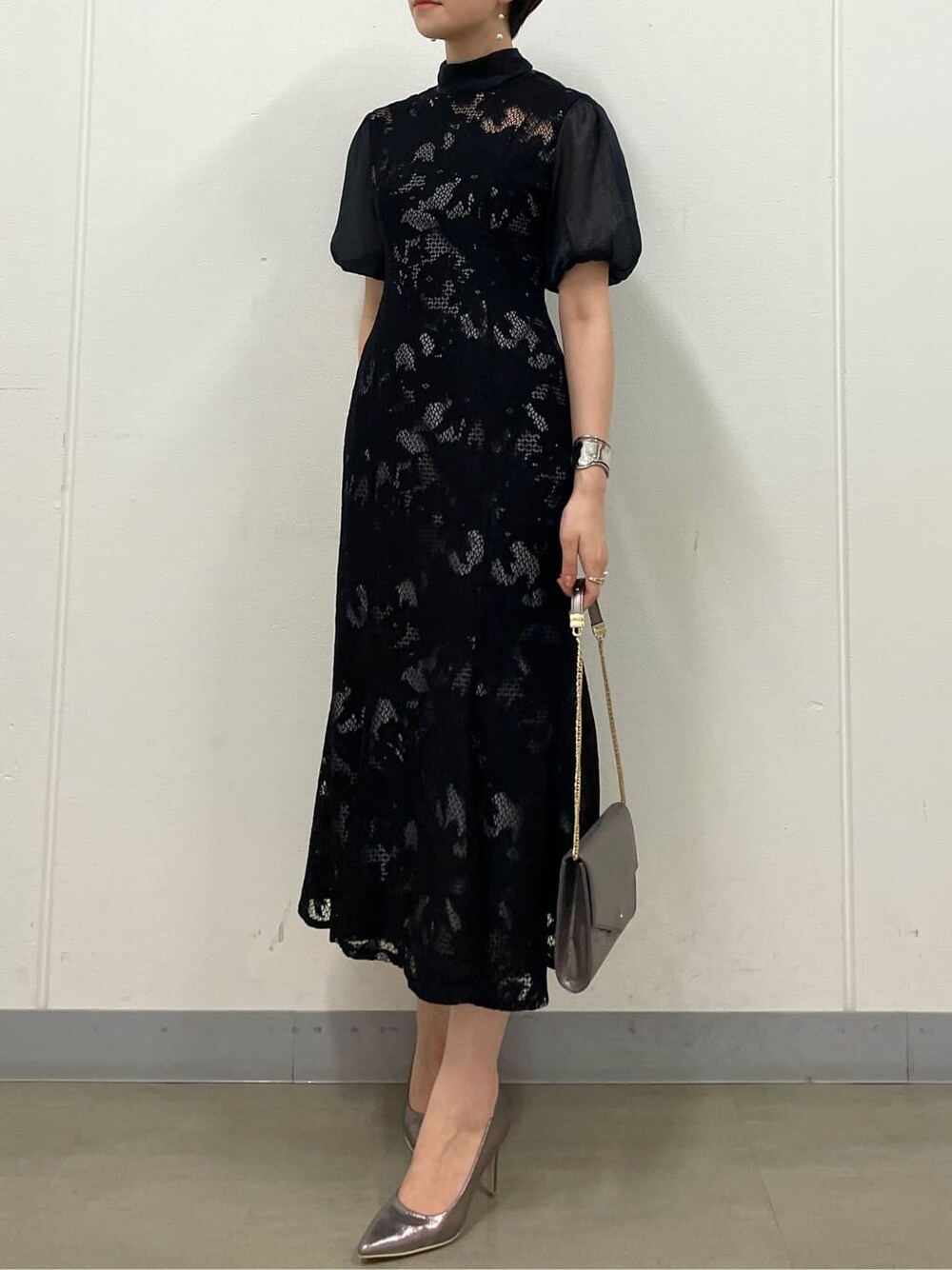 シルバー系のクラッチバッグ、シルバー系のパンプス、ブラック系のドレスを着用したレディースの夏コーディネートの4枚目の写真