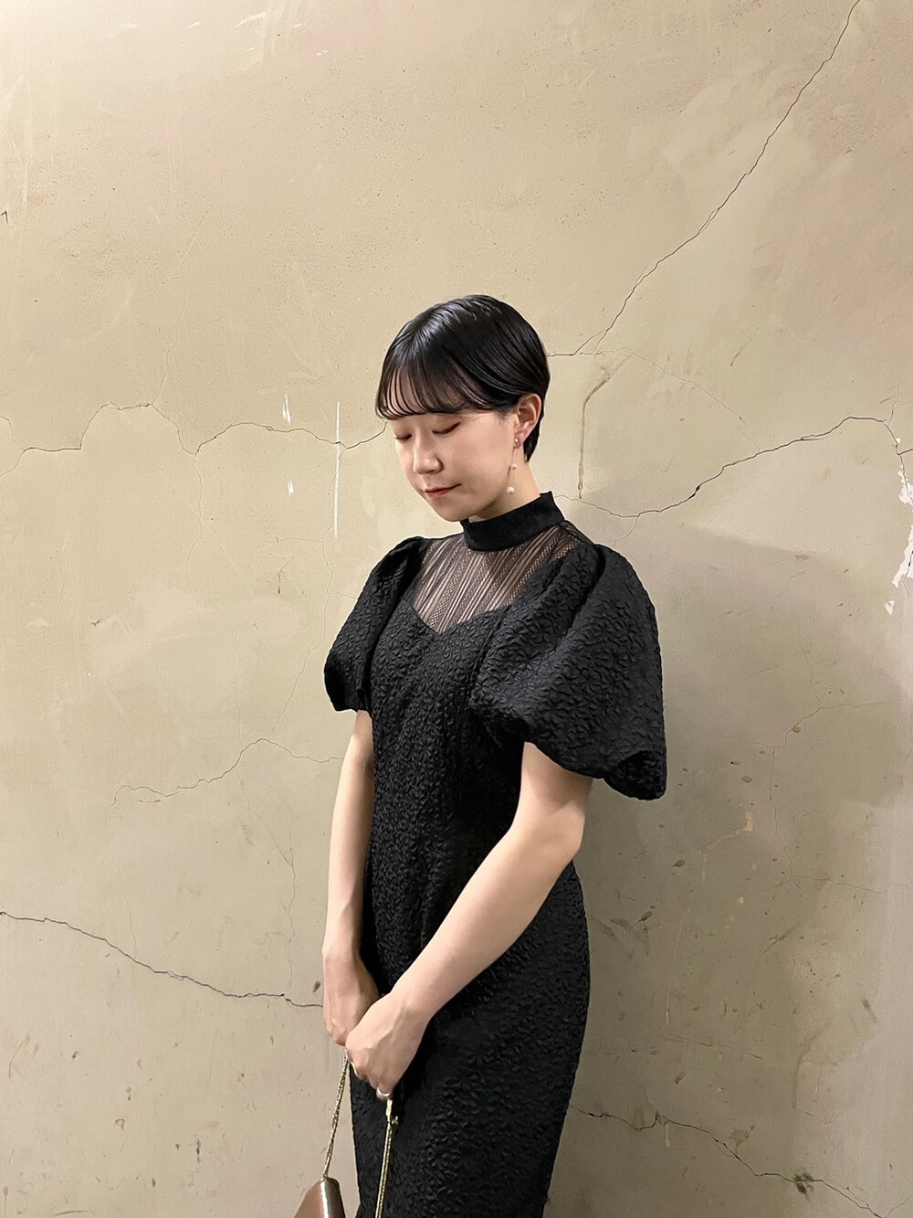 ブラック系のドレス、ゴールド系のハンドバッグ、ゴールド系のパンプスを着用したレディースの秋コーディネートの6枚目の写真