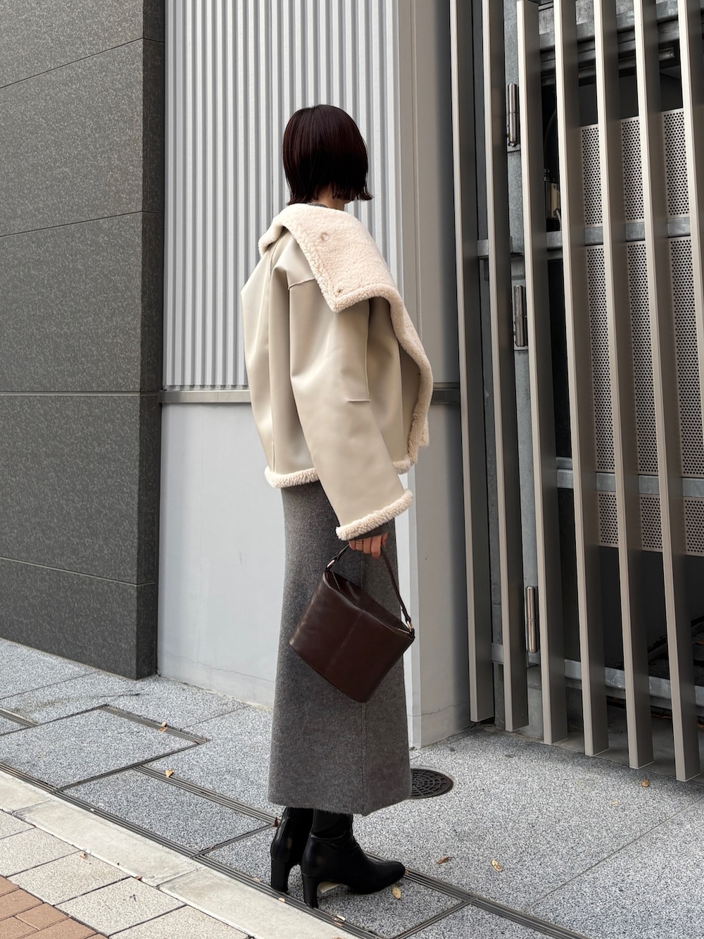 グレー系のワンピース、ブラウン系のハンドバッグ、ブラック系のブーツを着用したレディースの冬コーディネートの4枚目の写真