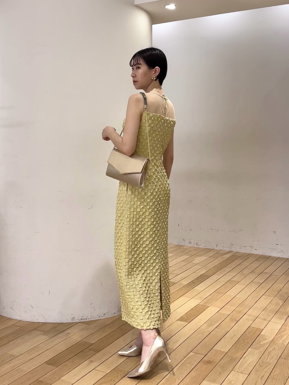 イエロー系のドレス、ゴールド系のパンプス、ゴールド系のクラッチバッグを着用したレディースの春コーディネートの7枚目の写真