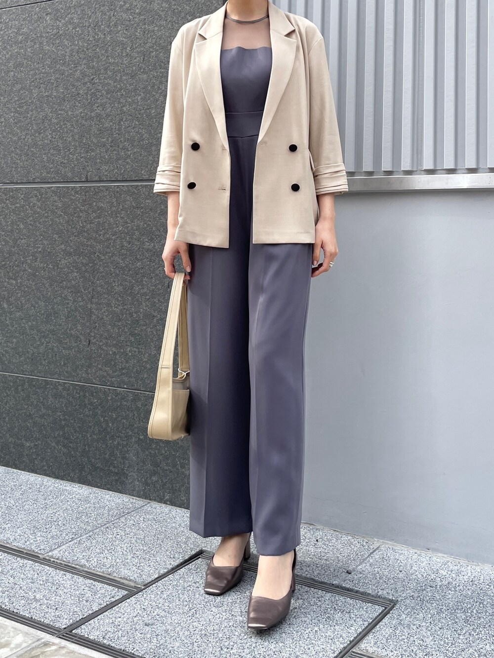 グレー系のパンツドレス、その他のパンプス、ベージュ系のテーラードジャケットを着用したレディースの春コーディネートの3枚目の写真