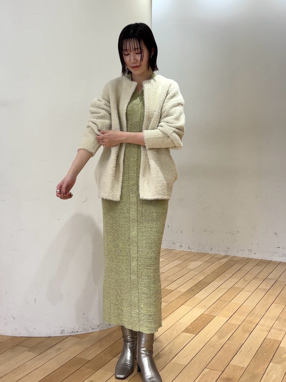 ホワイト系のカーディガン/ボレロ、グリーン系のワンピース、シルバー系のブーツを着用したレディースの冬コーディネートの2枚目の写真