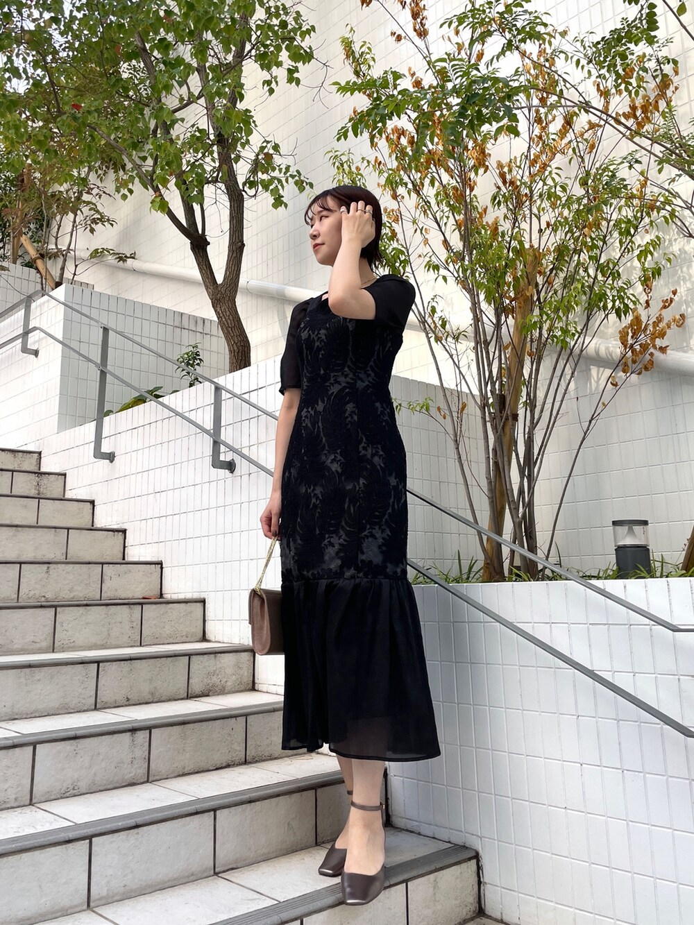 ゴールド系のハンドバッグ、その他のパンプス、ブラック系のドレスを着用したレディースの秋コーディネートの2枚目の写真