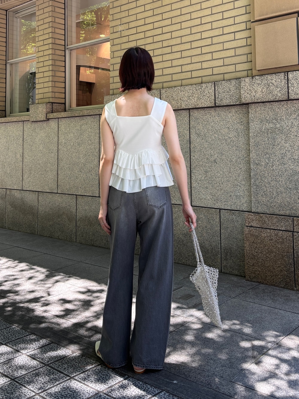 グレー系のデニムパンツ、ホワイト系のハンドバッグ、ホワイト系のサンダルを着用したレディースの春コーディネートの3枚目の写真