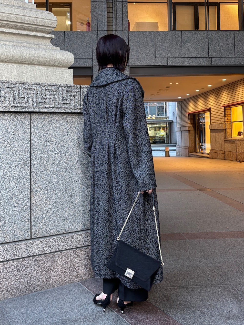 ブラック系のドレス、ブラック系のチェスターコート、ブラック系のハンドバッグを着用したレディースの冬コーディネートの3枚目の写真